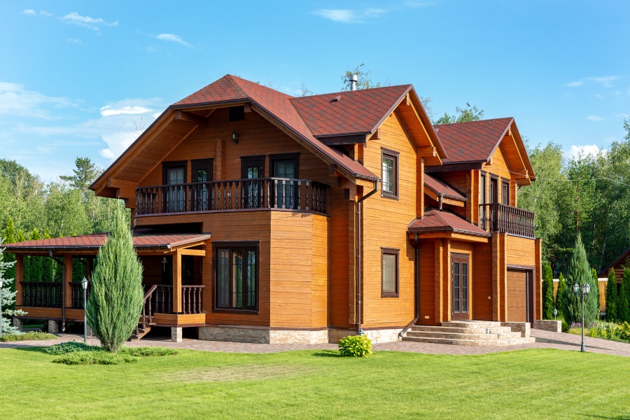 Beautiful luxury big wooden house. Timber cottage villa with with green lawn, garden and blue sky on background